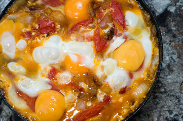 Scrambled eggs with tomatoes is prepared on a black pan on a metal lattice in the journey. The concept of the dish: a combination of protein and fiber