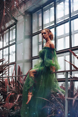 The girl elf sits on the fence in a chic dress in the garden