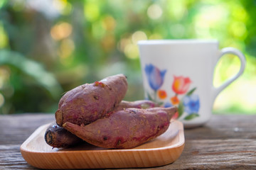 A cup of tea and red sweet potato on wooden plate over rustic wooden table