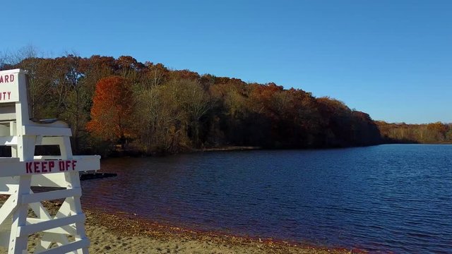 Aerial dolly past an empty lifeguard seat / platform at edge of a lake at fall
