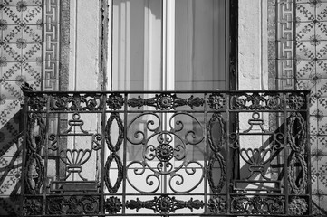 Rusty forging balcony and ceramic tiles (azulejos) wall. Architectural detail of typical old building in the centre of Lisbon (Portugal). Black and white photo..