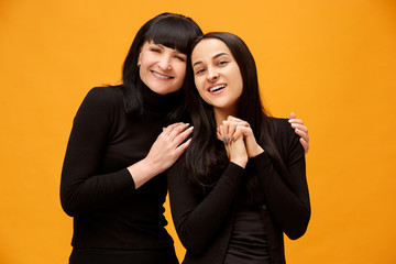 A portrait of a happy mother and daughter at studio on gold background. Trendy colors. Human positive emotions and facial expressions concept