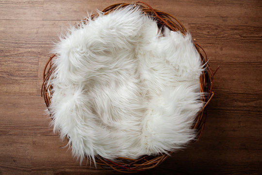 Wooden nest with white flufy sheepskin against an oak wooden floor