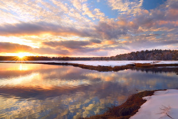 Winter sunset on the river and forest. Beautiful reflection of pink clouds in the water. USA....