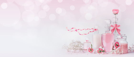 Various cosmetic glass bottles with pink ribbons and flowers standing on white pink background with bokeh, front view, banner or template. Skin care, cosmetic shop, sale and abstract beauty concept