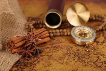 
Vintage compass with spyglass telescope and cinnamon spices on an old world map - trade and explorer concept