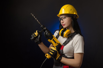 brunette girl in special clothes and a worker in a helmet posing on a black background with a working tool