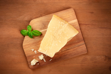 A piece of aged Parmesan cheese with crumbs and fresh basil, shot from the top on a dark rustic wooden background with a place for text