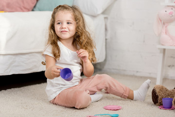 adorable kid playing with plastic cups on floor in children room