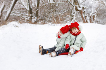 Fototapeta na wymiar Children twins are sitting on the snowy ground.
