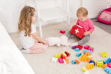 adorable sisters playing with toys on carpet in children room