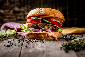Tasty fresh meat burger with cheese, tomato, onion and sauce served on wooden table. cooking fast...