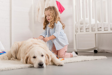 adorable kid with curly hair pretending veterinarian and examining golden retriever in children room