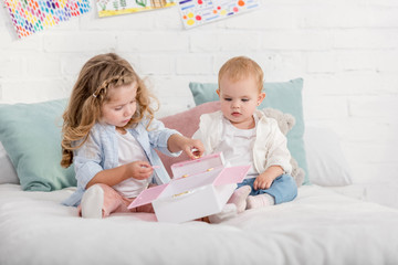 adorable preschooler and toddler sisters playing on bed in children room