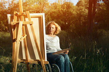 Woman in wheelchair drawing on easel outside
