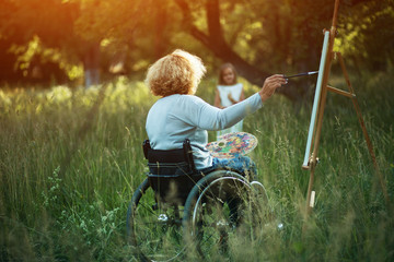 Woman in wheelchair drawing on easel outside