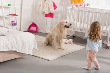 back view of kid walking to golden retriever in children room