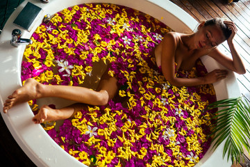 Young woman relaxing in flower bath,organic skin care, luxury spa hotel.Beauty body care top view.view from above sexy freelancer girl wellness treathment red, yellow, pink flowers petals in milk bath