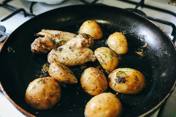 Chicken wings with potatoes lying on the frying pan on the oven. Homemade lunch. Unhealthy food photo with fat.