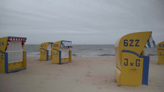 Moving shot towards the north sea / ocean leading through a few beach chairs on an overcast, cloudy day at the empty beach.