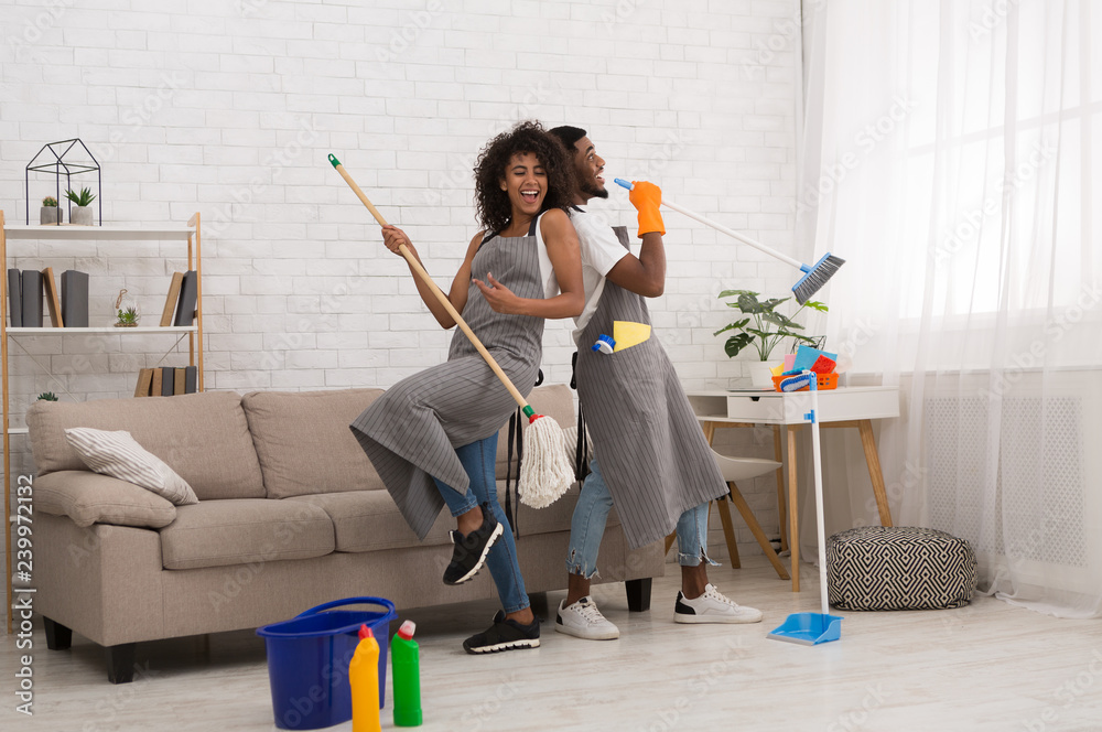 Wall mural Young couple cleaning home, having fun with mop and broom - Wall murals