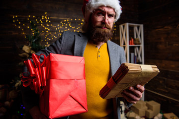 Fototapeta premium Man bearded hipster wear santa hat hold bunch of letters and gift box. Man mature bearded with eyeglasses received post for santa. Gifts delivery service. Letter for santa claus. Post for santa claus