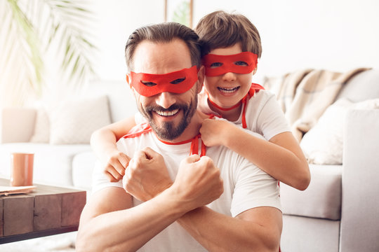 Father and son in superheroe costumes at home hugging looking camera happy team close-up