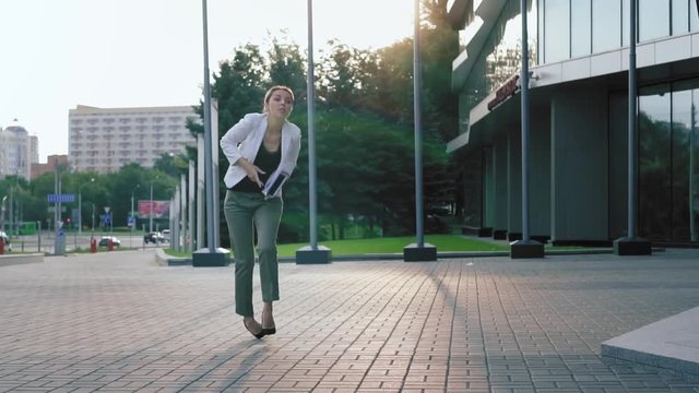 Business woman in high heels walks down the street, stumbles, drops documents, and puts them in order. Fail. Slow motion