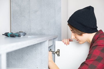 Woman adjusting furniture door at home. Female in casual shirt and knit hat does stereotypical men...