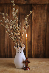 burning candle and willow branches on wooden background. Palm Sunday. Background mode, soft focus.