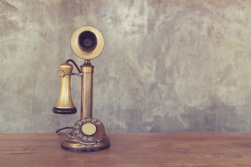 Vintage telephone on wooden table with cement wall background.