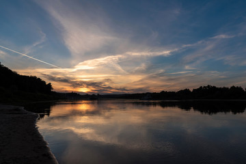 Sunset over the river and coastline. Beautiful sky blazes with fire. With white arrows. Romantic. Beautiful reflection in the water.