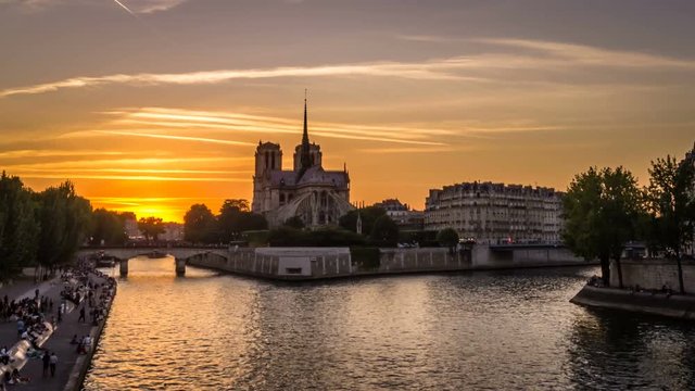 Timelapse of boats in Paris at sunset, with Notre-Dame-De-Paris church in the background and people resting on the docks, view from Tournelle bridge