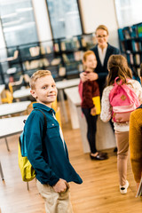 schoolboy with backpack looking at camera while visiting library with classmates
