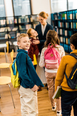 back view of schoolchildren with backpacks standing with librarian in library