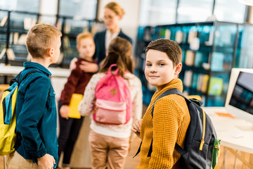 boy with backpack looking at camera while visiting library with classmates