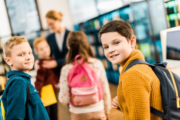 adorable schoolboys with backpacks looking at camera in library
