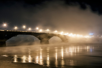 beautiful big bridge over the river in the fog, bright lights of the lanterns of the big city