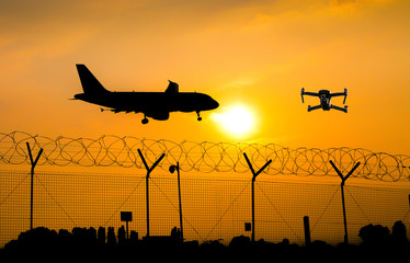 Unmanned drone flying over security fence at airport while commercial airplane prepares for landing, leading to possible collision - obrazy, fototapety, plakaty