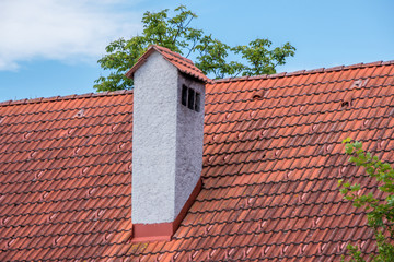 Old style concrete chimney at red clay bricks roof.
