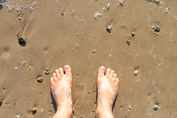 Male feet standing on the beach watching the water waves from above.