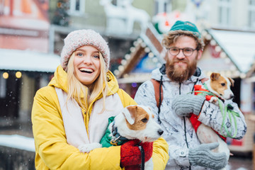 Excited loving hipster couple in bright warm clothes walking in a winter city with two dogs Jack...