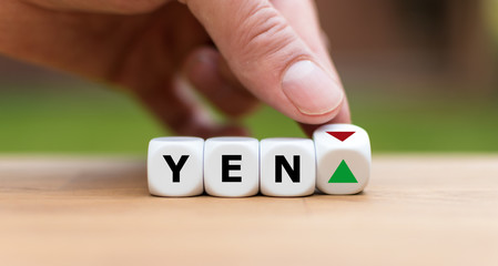 Hand is turning a dice and changes the direction of an arrow symbolizing that the value of the Yen...