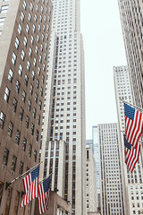 low angle view of skyscrapers and american flags on new york city street, usa