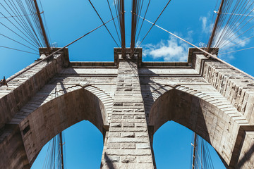 bottom view of brooklyn bridge against blue cloudy sky background in new york, usa
