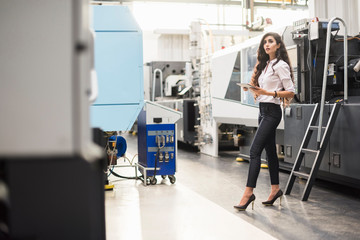 Woman with tablet at machine in factory shop floor looking around