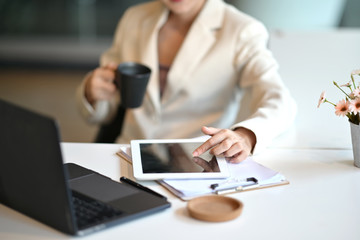 Young businesswoman sitting at her desk in an office reading report on tablet