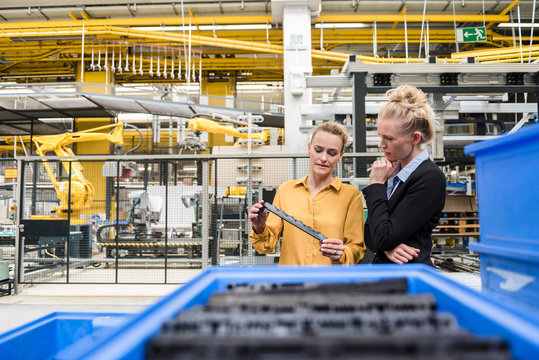 Two women examining workpiece in factory