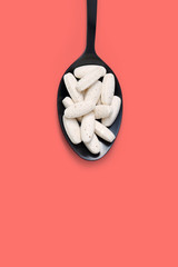 Multivitamin tablets on black spoon against pink color background