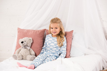 adorable child sitting on bed with teddy bear